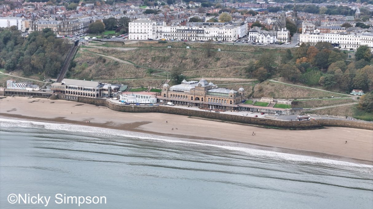 Coastal view of a beach with buildings and greenery in the background.