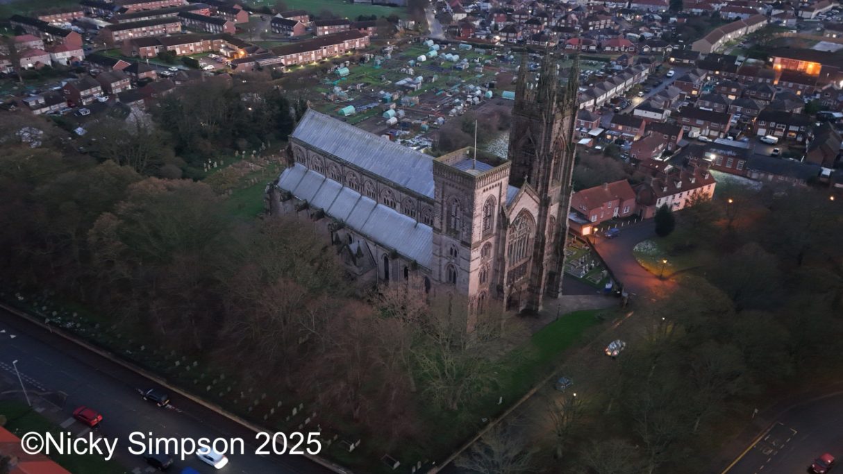 Aerial view of a church surrounded by trees and houses at dusk.