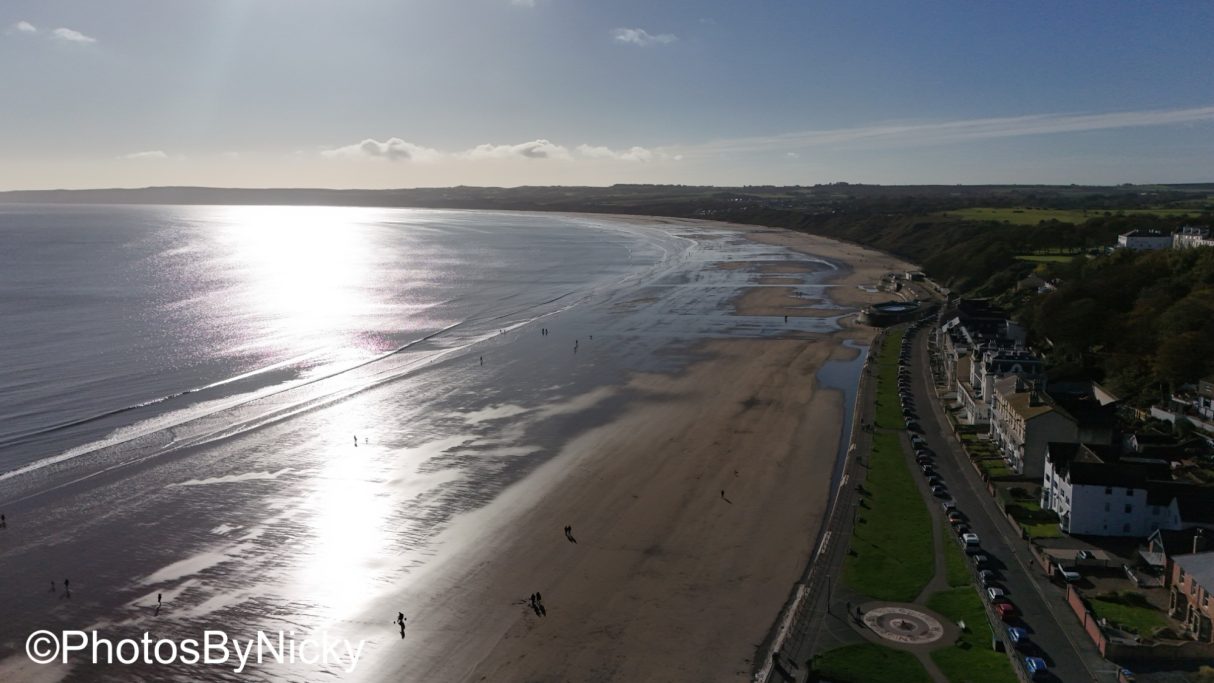 Aerial view of a sandy beach with shimmering water under a clear blue sky.