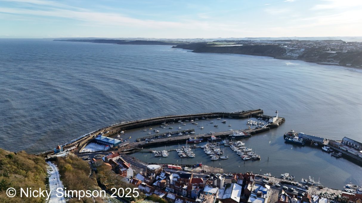 A coastal view of a marina with moored boats and a calm sea beyond.