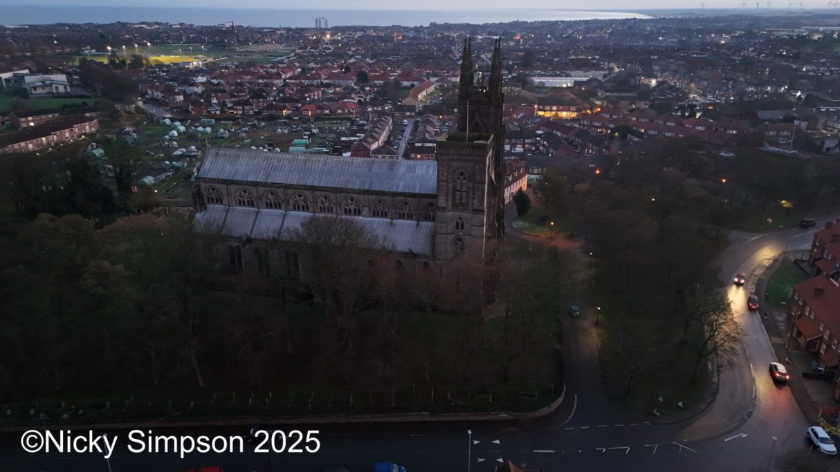 Aerial view of a town at dusk, featuring a church and surrounding buildings.