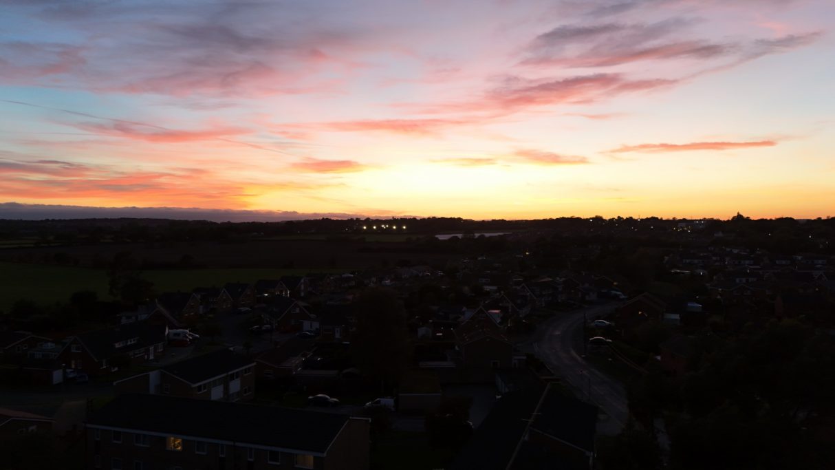 Colourful sunset over houses and fields, with vibrant pink and orange hues in the sky.