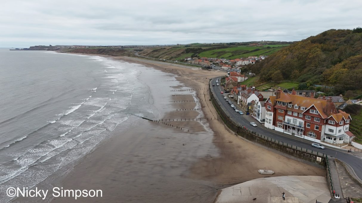 A coastal view with a sandy beach, waves, and seaside buildings along the shore.