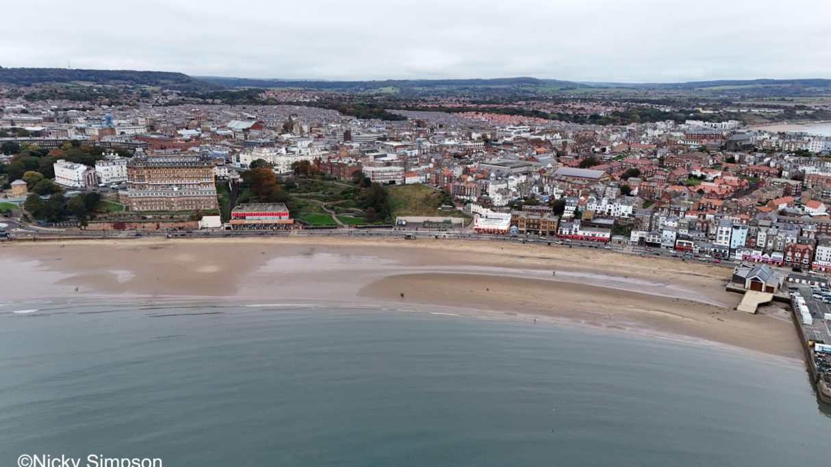 Aerial view of a beach beside a town with buildings and a cloudy sky.