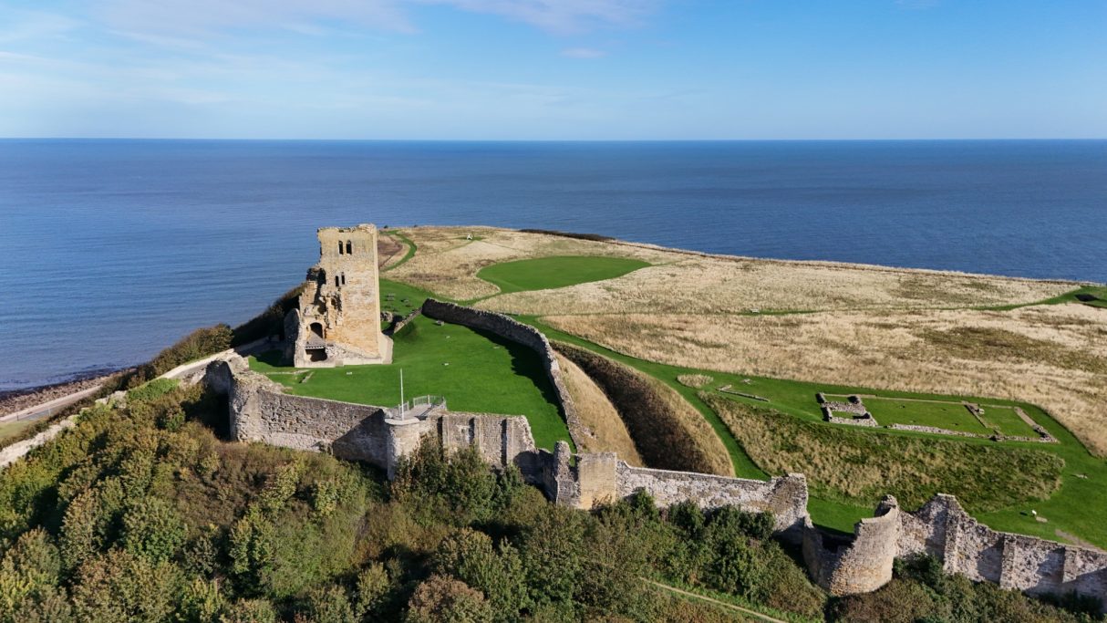 Coastal view of an ancient castle ruins overlooking the sea and grassy landscape.