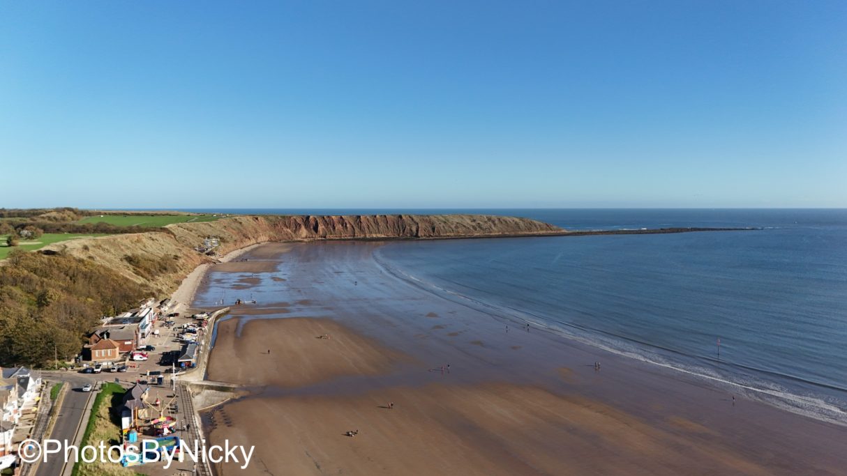 A coastal view with a beach, cliffs, and clear blue sky.