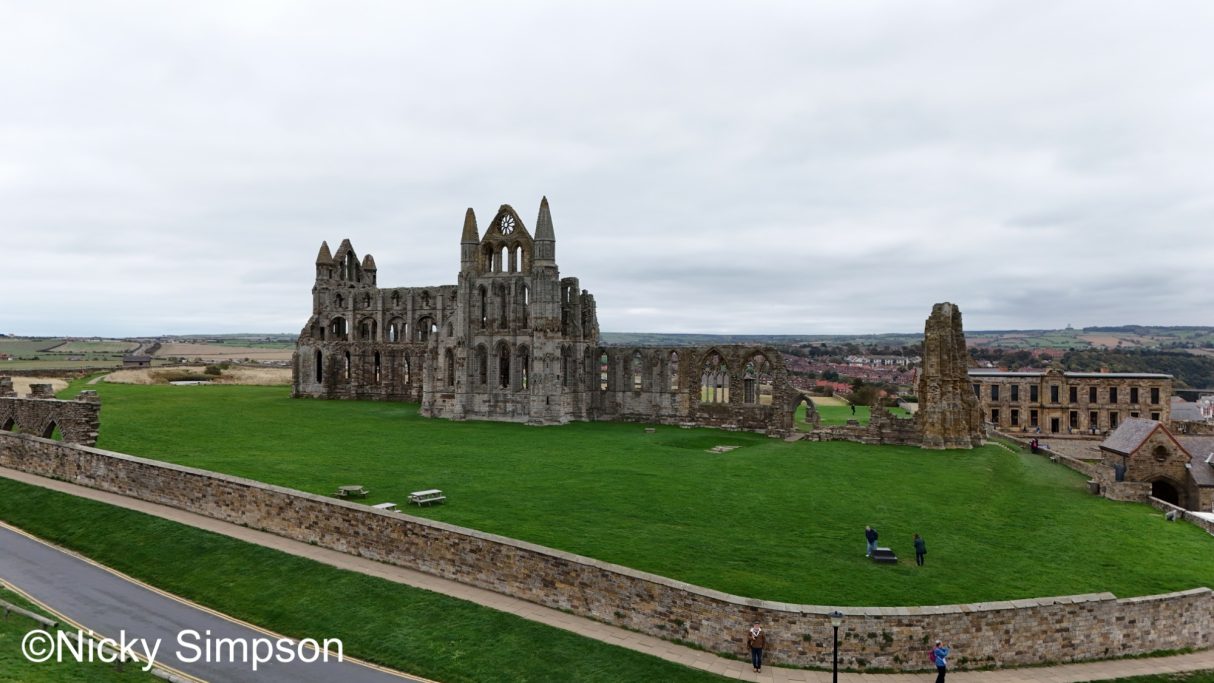 Ruins of Whitby Abbey on green grass under a cloudy sky.