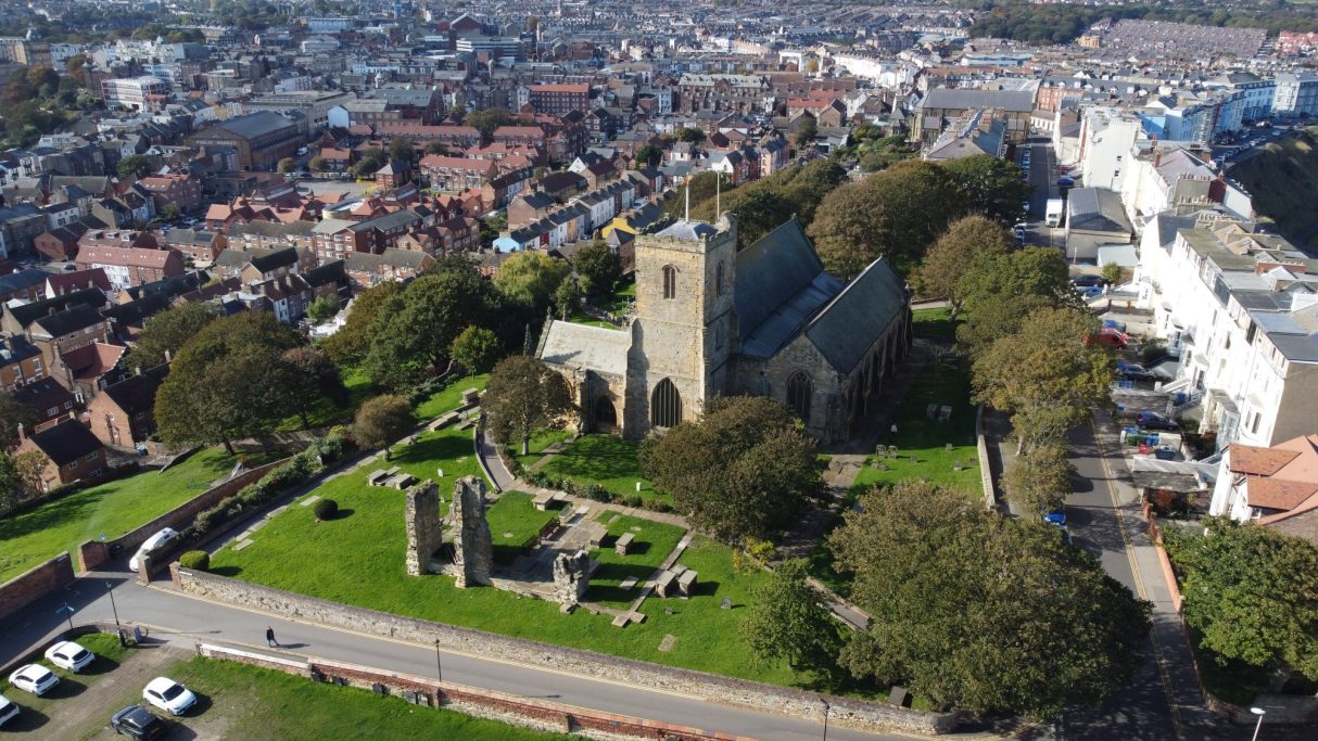 Drone view of a church with surrounding gardens and nearby urban buildings.