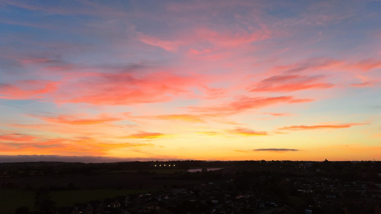 A vibrant sunset with pink and orange clouds over a landscape silhouette.