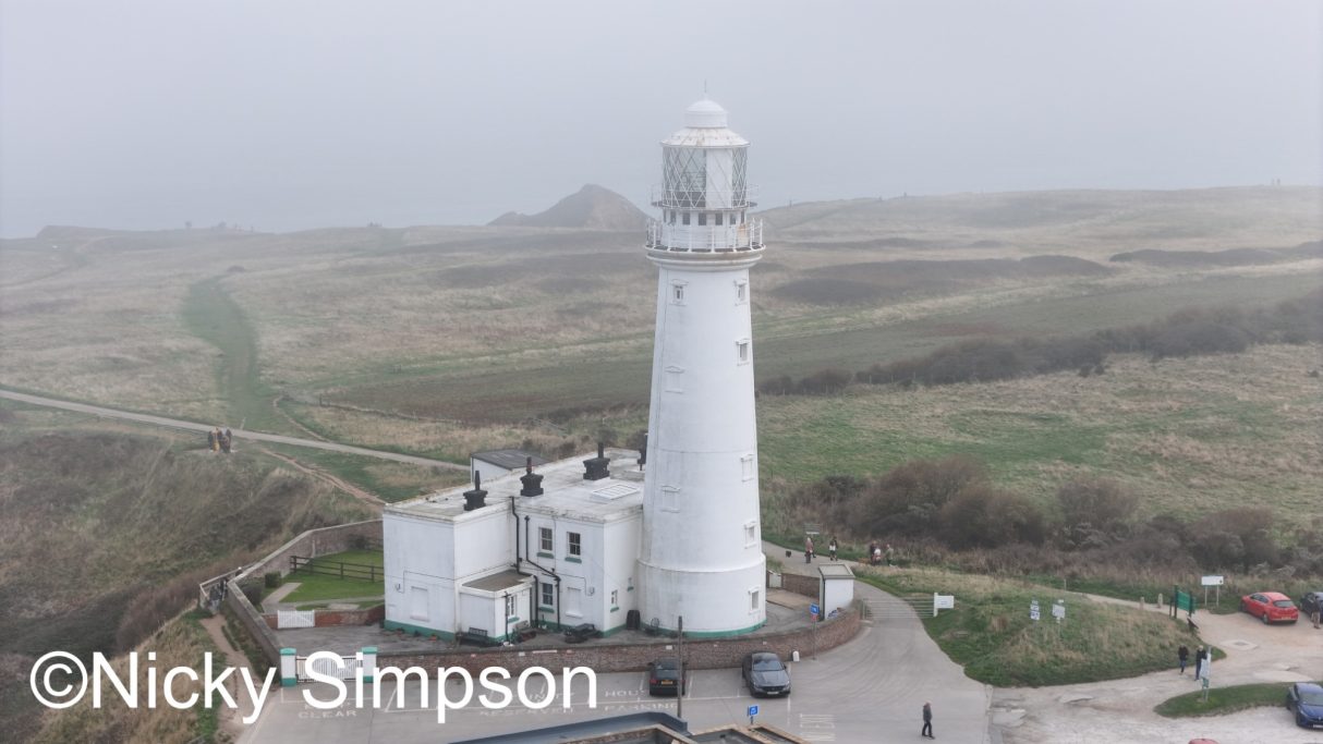 A tall white lighthouse surrounded by mist and grasslands.