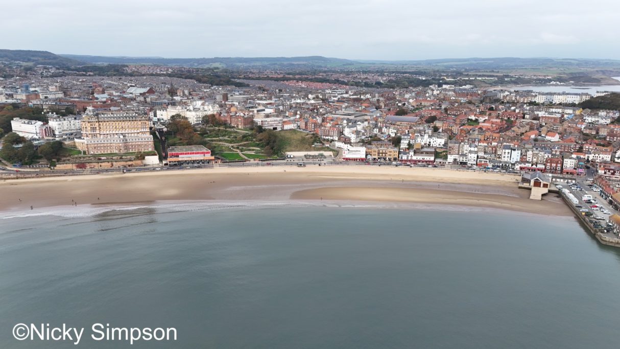 Aerial view of a coastal town with sandy beach and buildings along the shoreline.