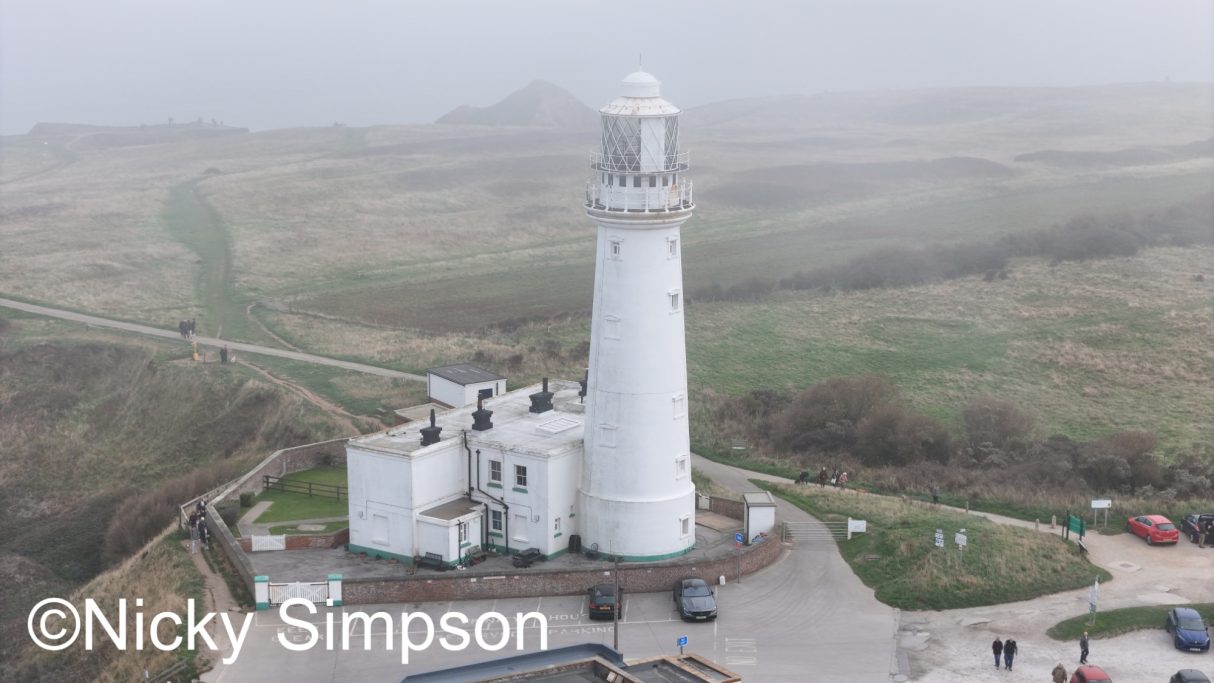White lighthouse on a foggy coastline surrounded by green fields.