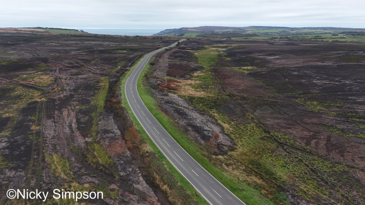 Winding road through a barren landscape with patches of green and rocky terrain.